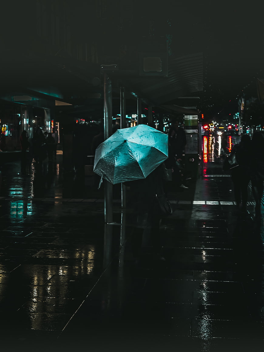 Person with Blue Umbrella on Rainy City Street at Night