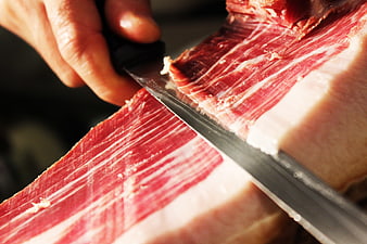 Close-up of hand slicing Spanish Iberico ham with knife