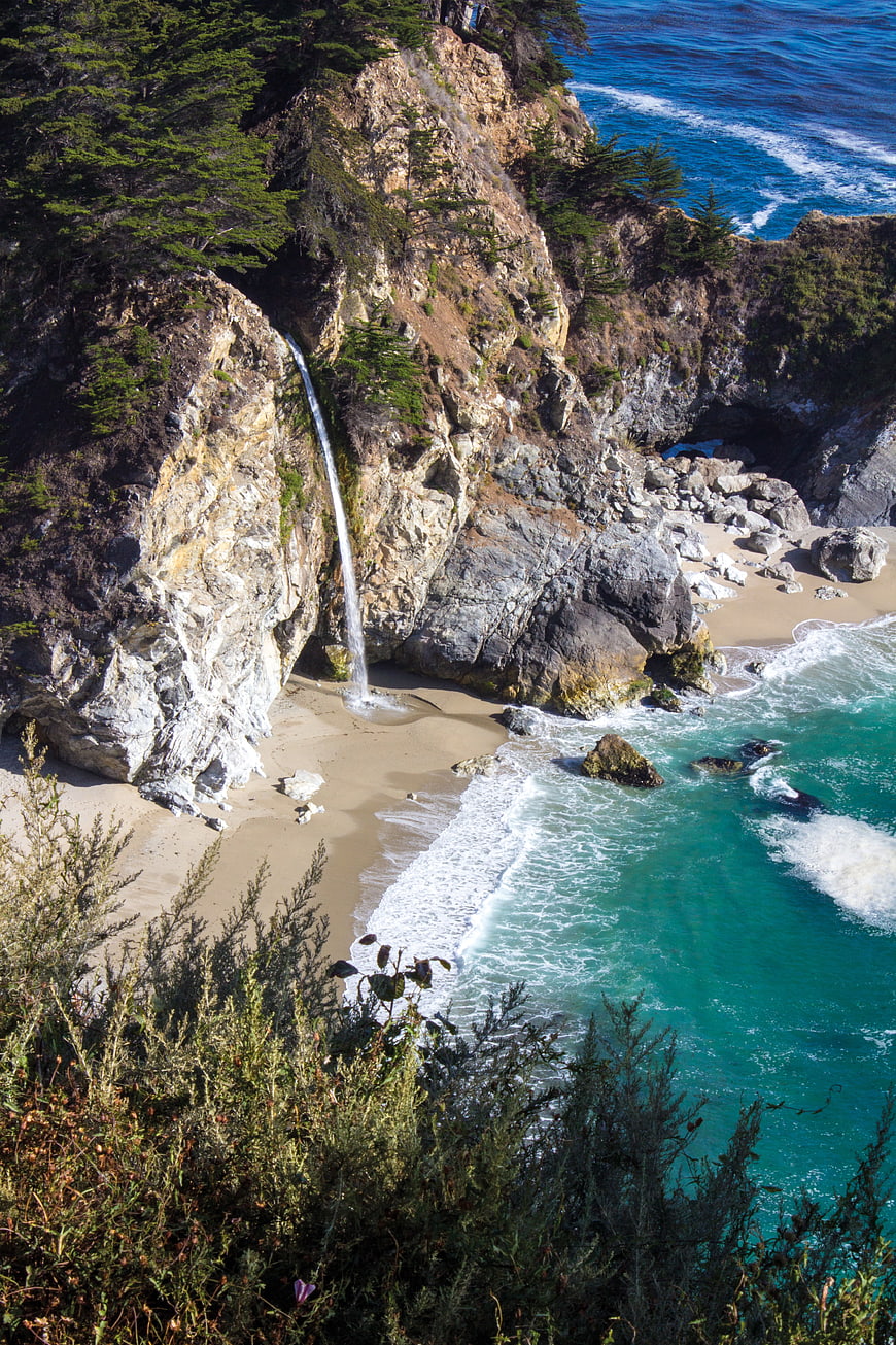 Hidden Coastal Waterfall Pouring Into Turquoise Sea On Rocky Beach