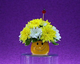 Yellow and white chrysanthemums in a smiley face vase