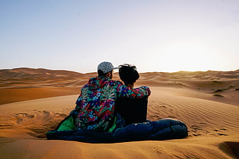 Couple sitting on sand dunes watching sunset in desert