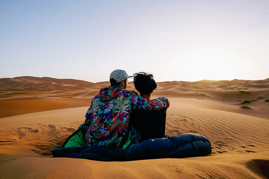 Couple sitting on sand dunes watching sunset in desert