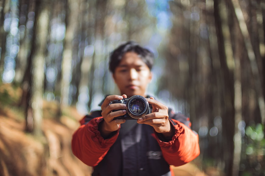 Man holding camera in forest with shallow depth of field