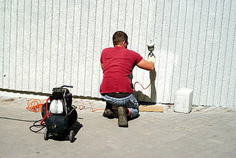 Man Using Airless Paint Sprayer On White Wall