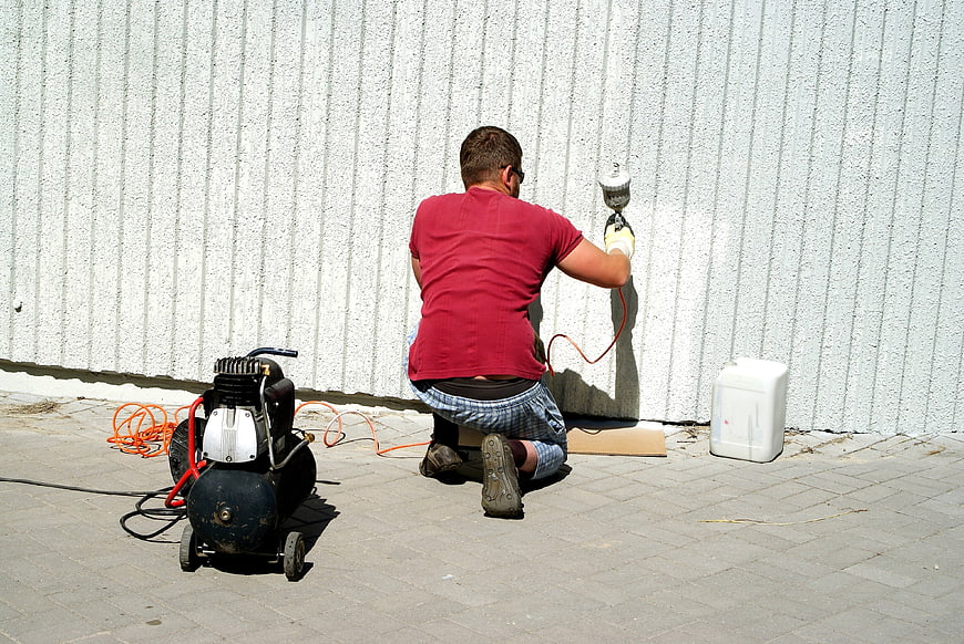 Man Using Airless Paint Sprayer On White Wall