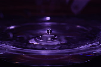 Purple water droplet splash with ripples in dark liquid