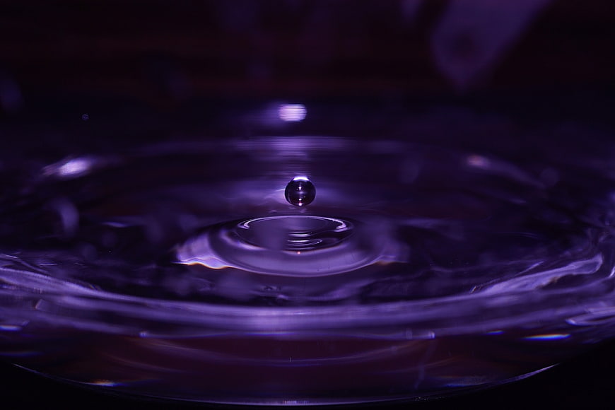 Purple water droplet splash with ripples in dark liquid