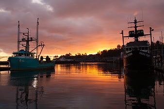 Fishing boats docked in harbor at sunset with orange sky