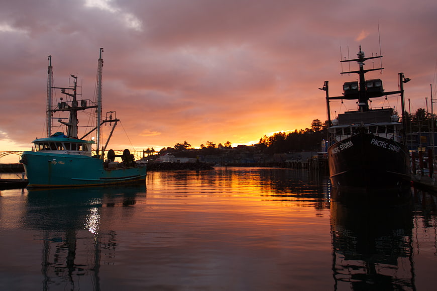 Fishing boats docked in harbor at sunset with orange sky