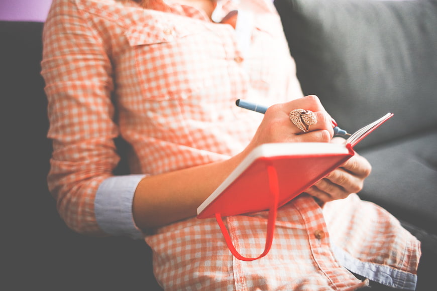 Woman Writing in Red Notebook on Couch