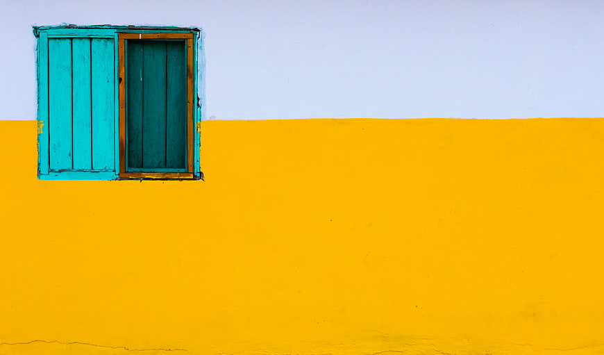 Minimalist yellow wall with turquoise window shutter