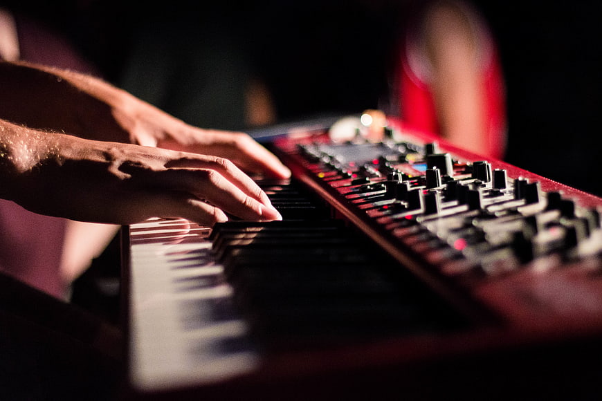 Close-up of hands playing a red synthesizer keyboard