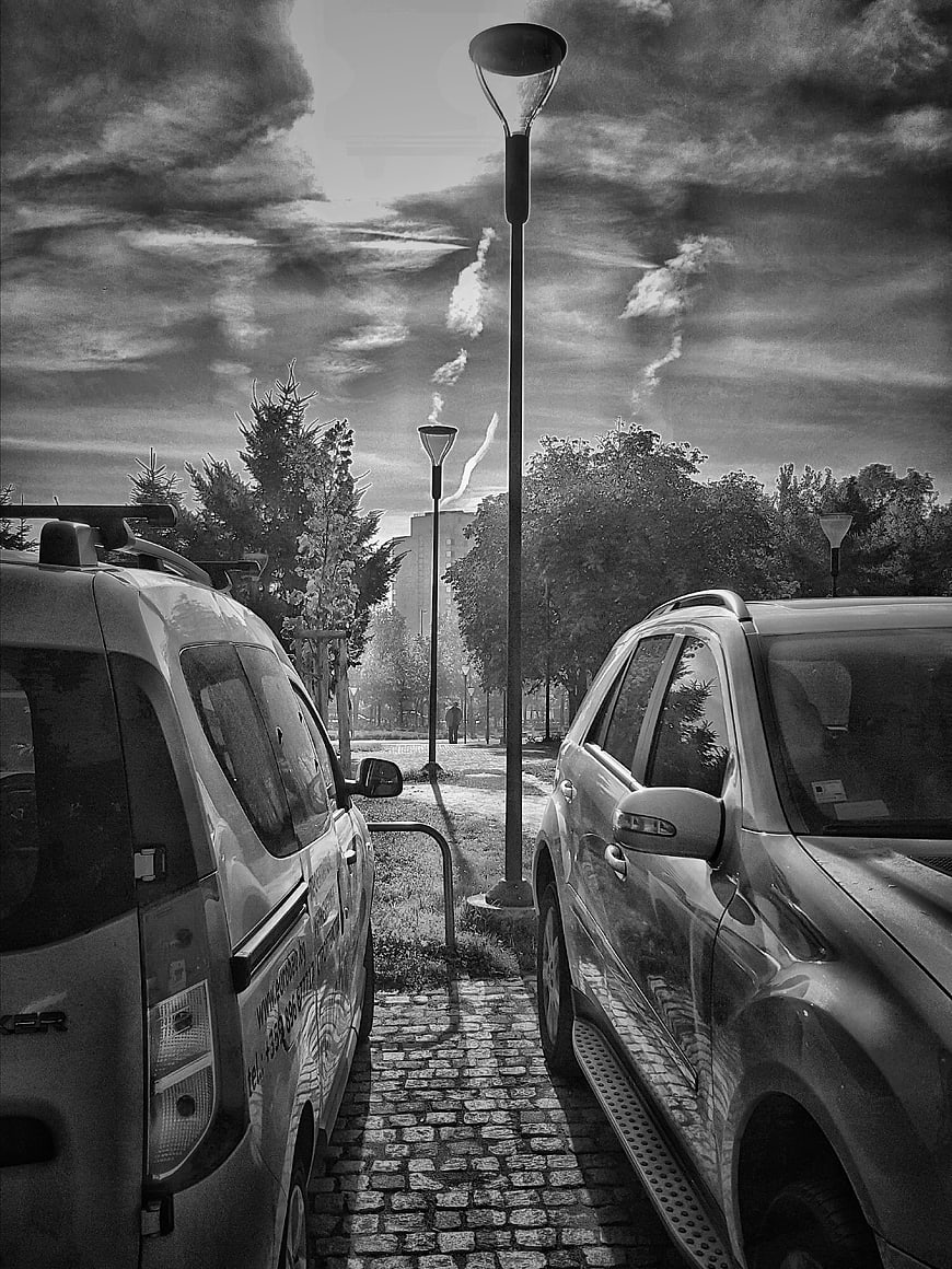 Black and white street scene with parked cars and dramatic clouds