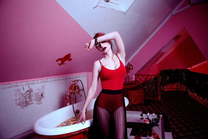 Woman in red dress posing by vintage bathtub in pink room