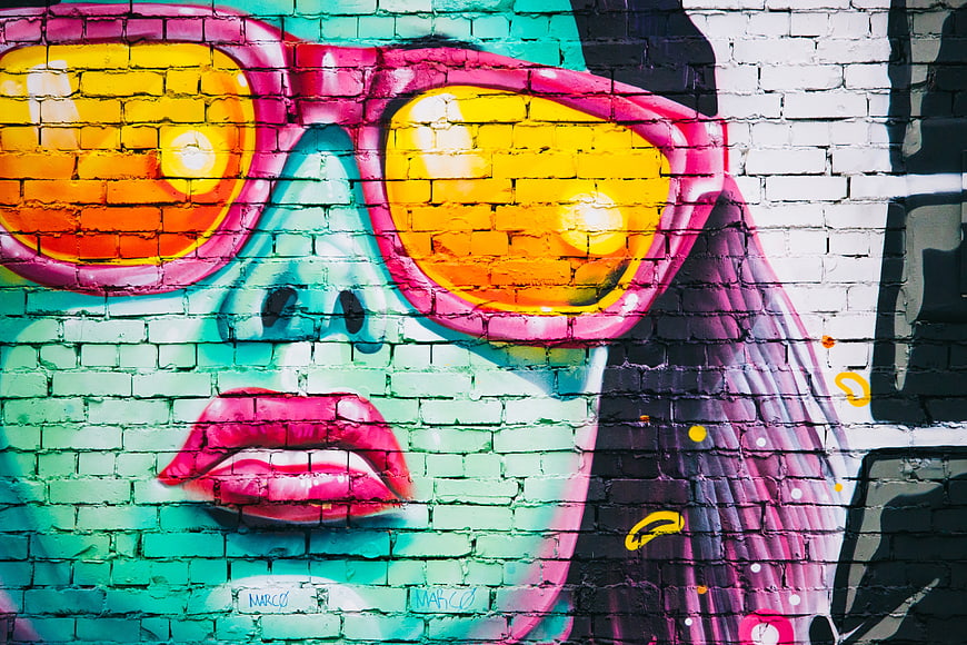 Colorful street art mural of woman with sunglasses on brick wall