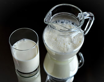 Fresh milk in glass and pitcher on black background