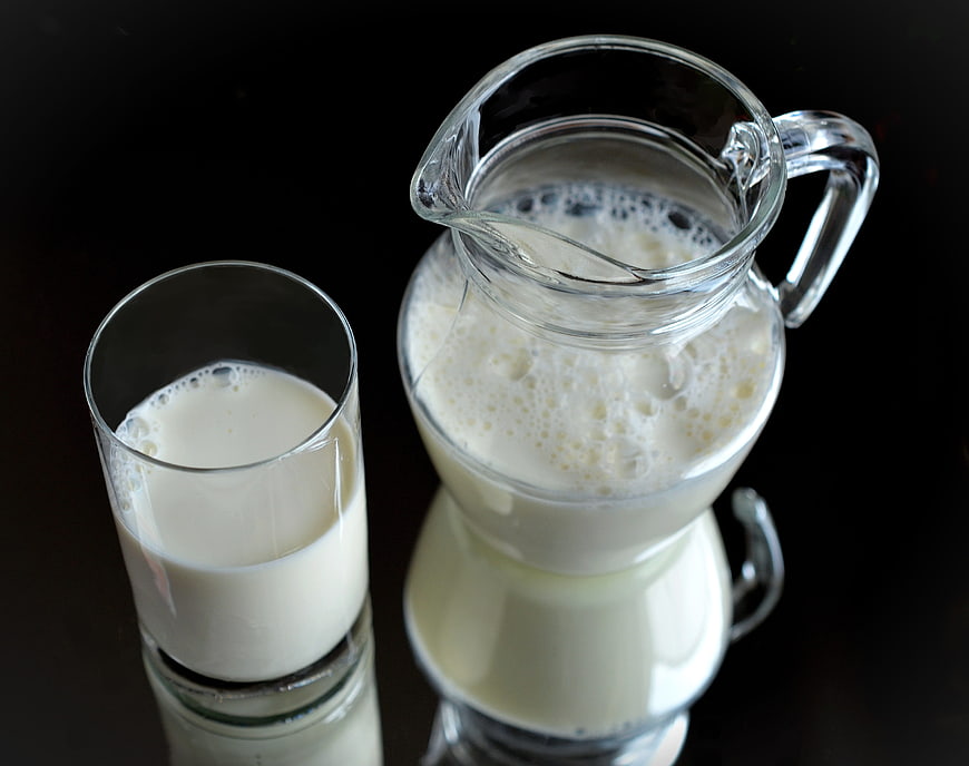 Fresh milk in glass and pitcher on black background
