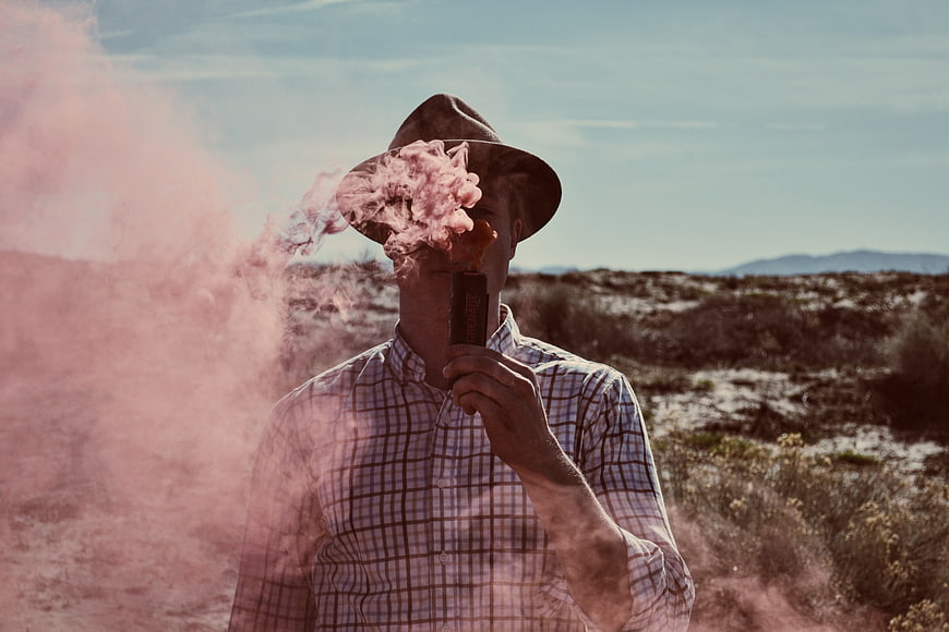 Man in Hat Holding Pink Smoke Grenade in Desert
