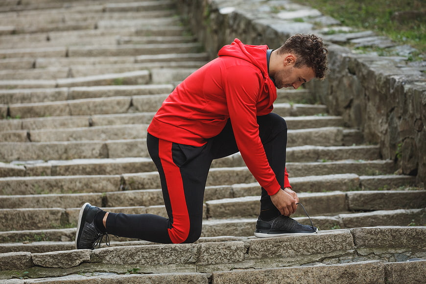 Athletic man tying shoelaces on stone steps