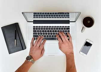 Top view of hands typing on laptop with coffee and notebook