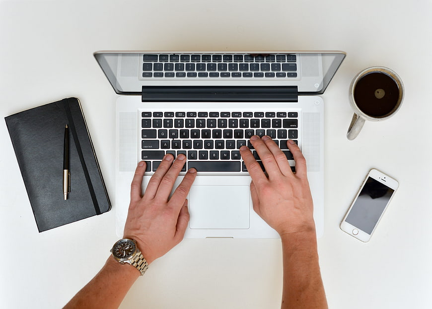 Top view of hands typing on laptop with coffee and notebook