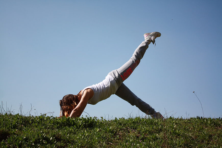 Woman doing yoga pose on grassy hill against blue sky
