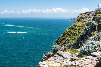 Scenic coastal cliff view with blue ocean and sailboats