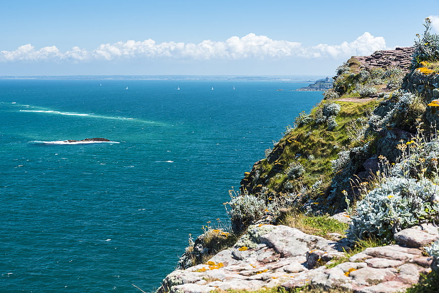 Scenic coastal cliff view with blue ocean and sailboats