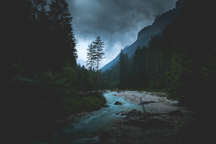 Dramatic Alpine River Flowing Through Dark Forest