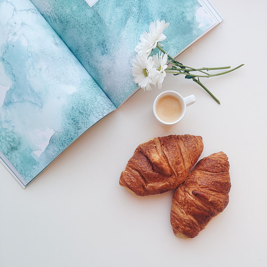 Flat lay of croissants, coffee, and blue watercolor book