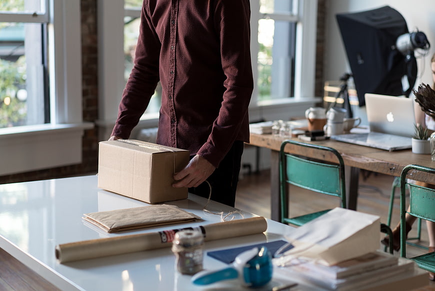 Person packing cardboard box for shipping in office workspace