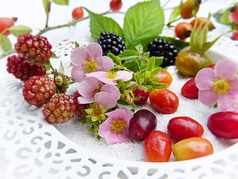 Fresh wild berries, flowers, and sugar on white plate