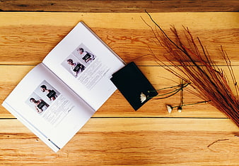 Flat lay of open magazine, black notebook, and dried flowers on wood