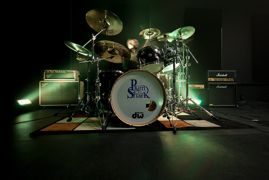 Drummer performing on stage with green lighting and amplifiers
