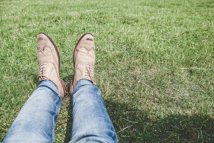Man's legs in jeans and brown shoes on green grass