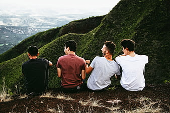 Four male friends sitting on a mountain ridge overlooking a valley