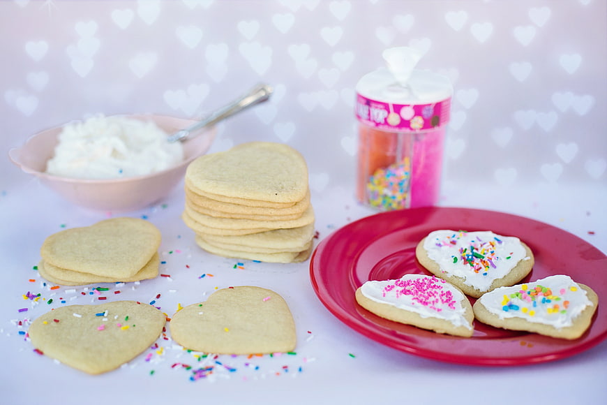 Heart-Shaped Sugar Cookies With White Icing And Sprinkles On Red Plate