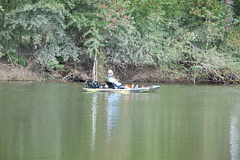 Man fishing from kayak on calm river near forest