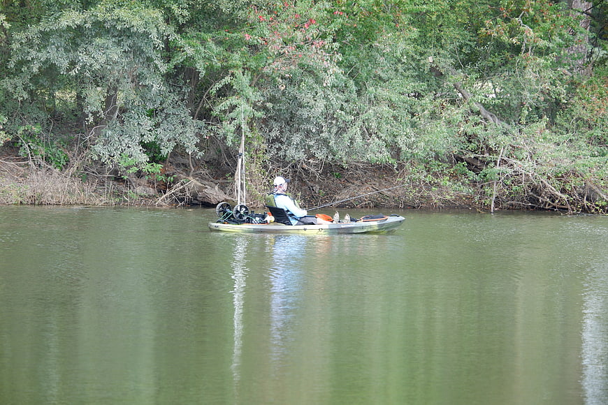 Man fishing from kayak on calm river near forest