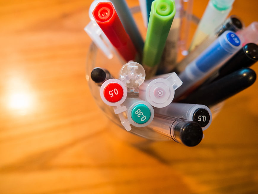Close-up of colorful pens in a glass cup on a wooden desk