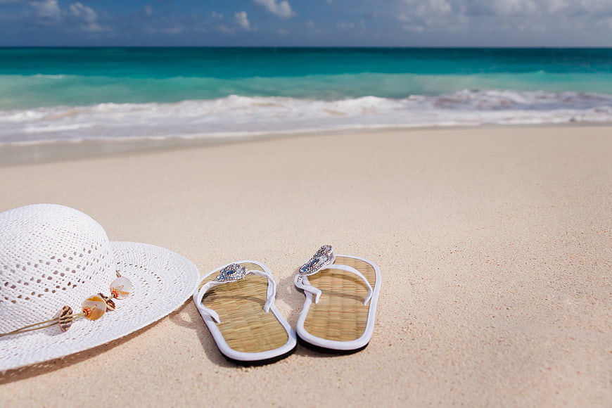 White straw hat and sandals on sandy beach with turquoise ocean