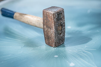Rusty hammer resting on cracked blue glass surface