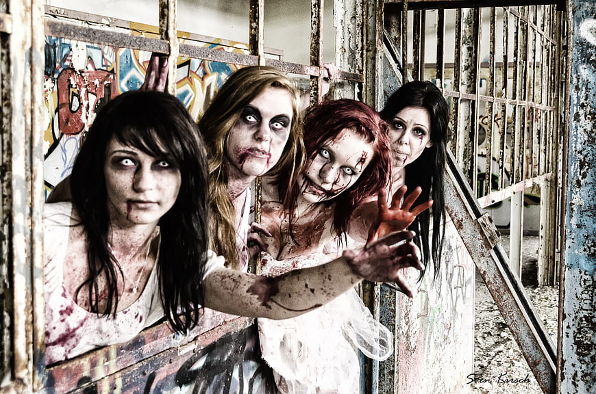 Group of female zombies reaching through rusty bars