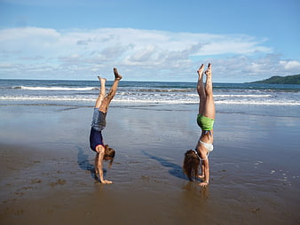 Two Women Performing Handstands on Wet Sandy Beach