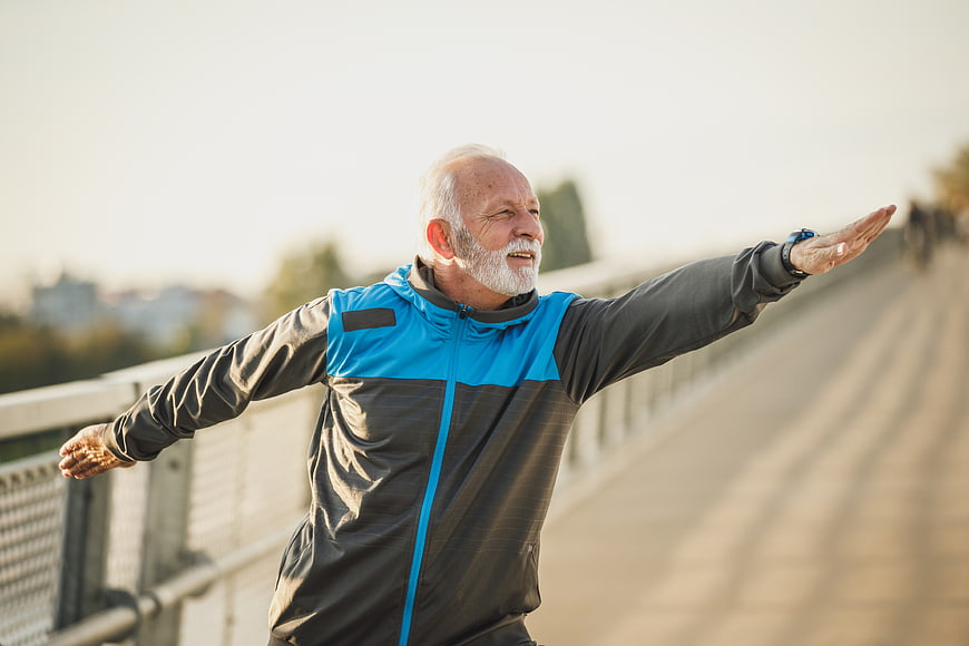 Senior man stretching arms outdoors on bridge