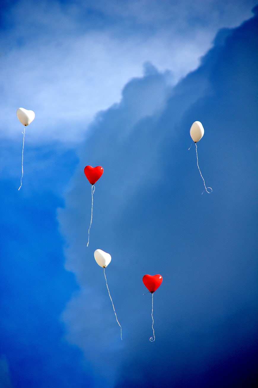 Five Heart-Shaped Balloons Floating Against Dramatic Blue Sky