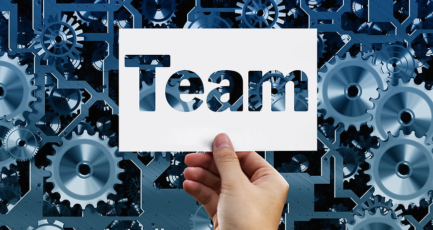 Hand holding white card with Team text against blue mechanical gears background