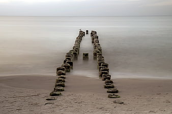 Wooden Breakwater Leading Into Calm Sea On Sandy Beach