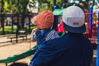 Father holding toddler at playground from behind