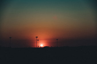 Silhouette of stadium lights against a grainy sunset sky